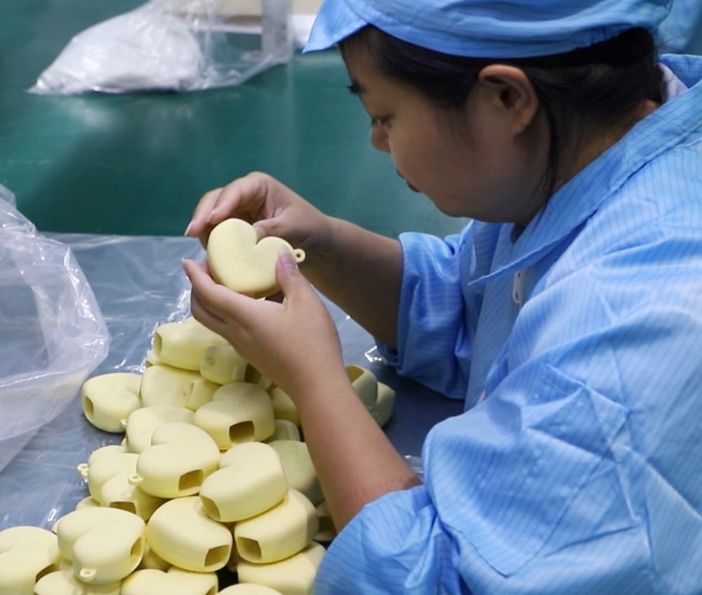 Factory worker inspecting heart-shaped custom silicone products during quality control process.