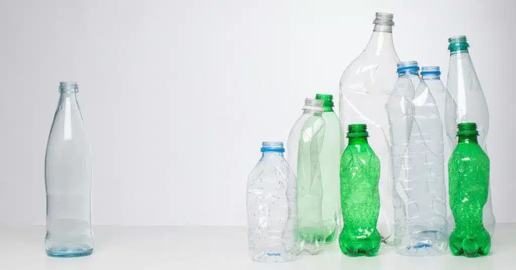 Plastic bottles of different sizes contrasted with reusable glass to emphasize sustainability concerns.